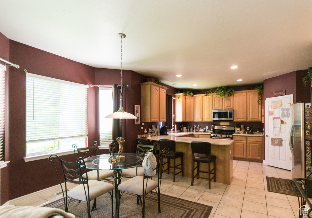Kitchen with appliances with stainless steel finishes, a peninsula, light countertops, light tile patterned floors, and a breakfast bar area