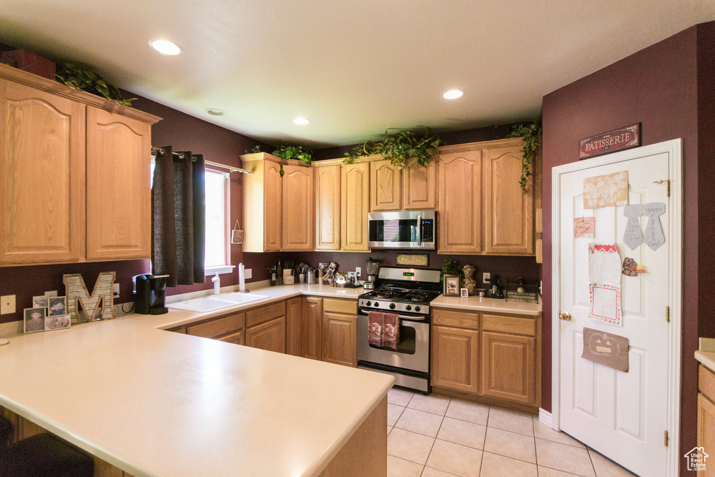 Kitchen featuring appliances with stainless steel finishes, a sink, a peninsula, light countertops, and recessed lighting