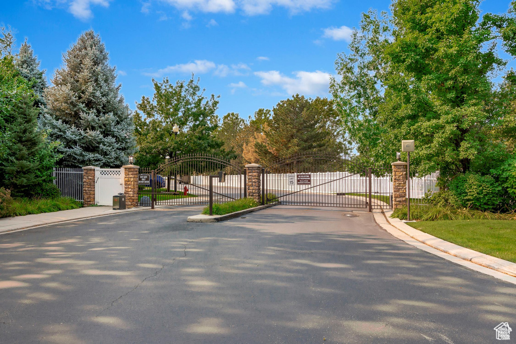 View of asphalt road featuring a gate, a gated entry, and curbs