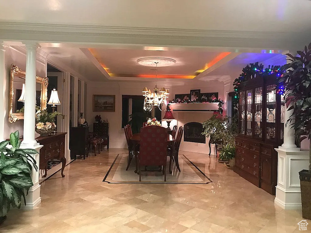 Dining area featuring a chandelier, a raised ceiling, decorative columns, crown molding, and a fireplace