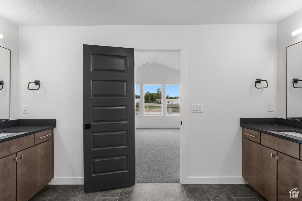 Bathroom with baseboards, two vanities, a textured ceiling, and lofted ceiling