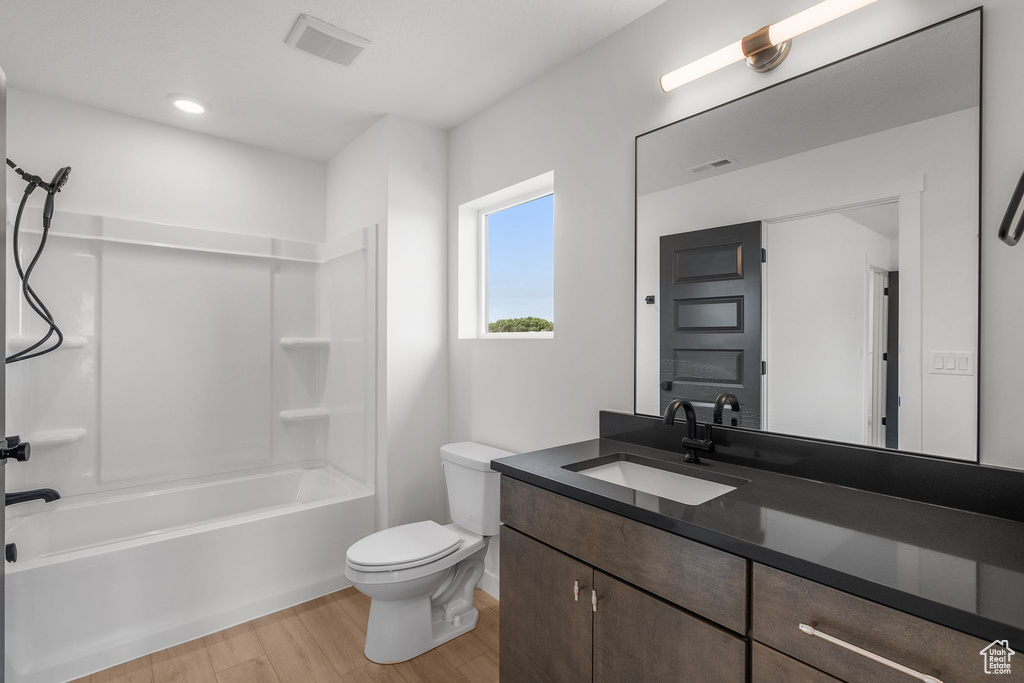 Bathroom with wood finished floors, toilet, vanity, shower / washtub combination, and baseboards