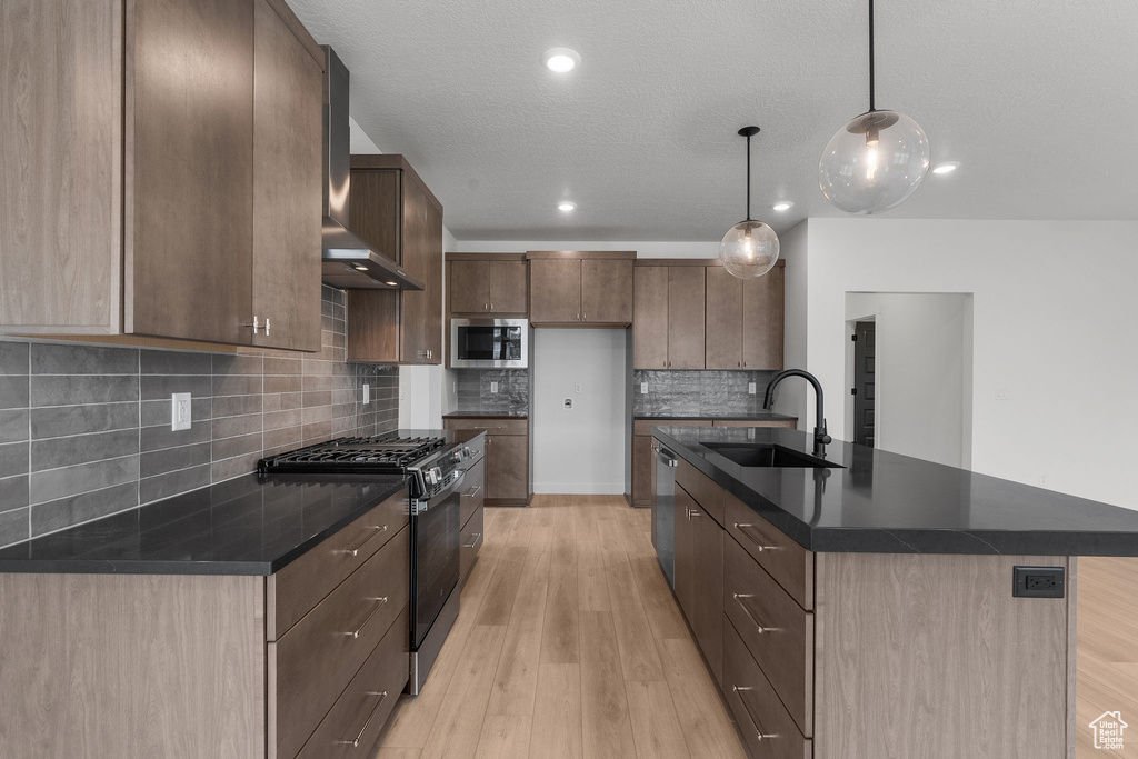 Kitchen featuring appliances with stainless steel finishes, a sink, dark countertops, wall chimney exhaust hood, and recessed lighting