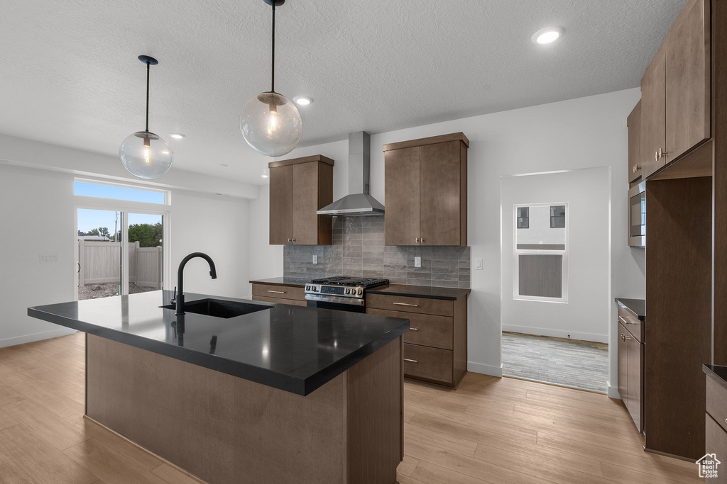 Kitchen featuring wall chimney range hood, a sink, stainless steel appliances, dark countertops, and light wood-type flooring