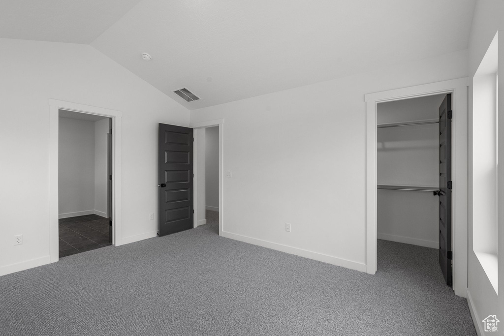 Unfurnished bedroom with a spacious closet, lofted ceiling, carpet floors, and baseboards