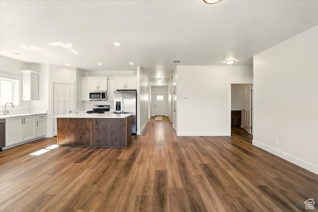 Kitchen with stainless steel appliances, a center island, white cabinetry, a sink, and dark wood-style floors