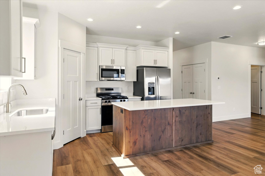 Kitchen featuring stainless steel appliances, a sink, dark wood-style floors, white cabinetry, and a center island