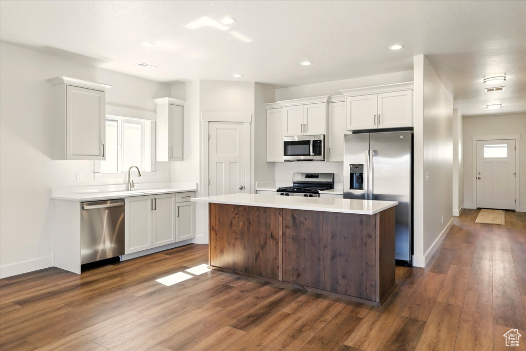 Kitchen with stainless steel appliances, white cabinetry, dark wood-style flooring, light countertops, and baseboards
