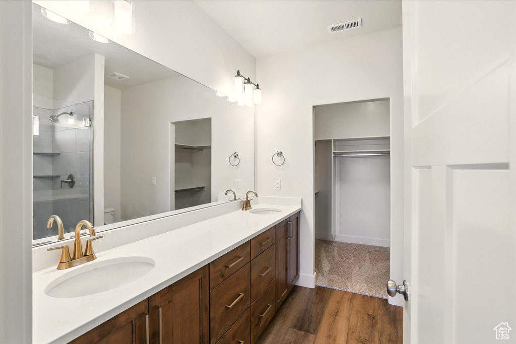 Full bath featuring double vanity, a walk in closet, toilet, wood finished floors, and a shower