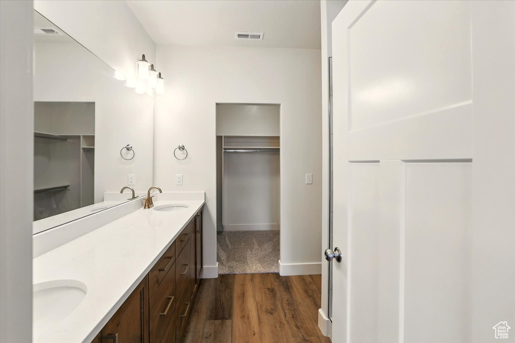 Bathroom featuring wood finished floors, double vanity, a walk in closet, and baseboards