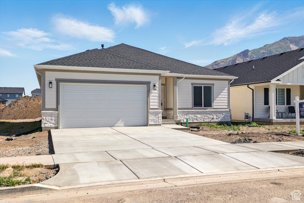 Single story home with driveway, an attached garage, a mountain view, stone siding, and a porch