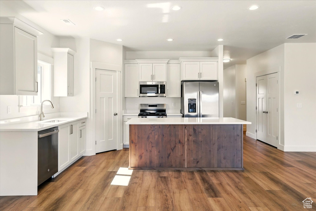 Kitchen with stainless steel appliances, a center island, dark wood-type flooring, white cabinets, and recessed lighting