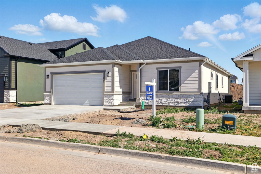 View of front of property featuring central AC unit, a garage, driveway, and stone siding