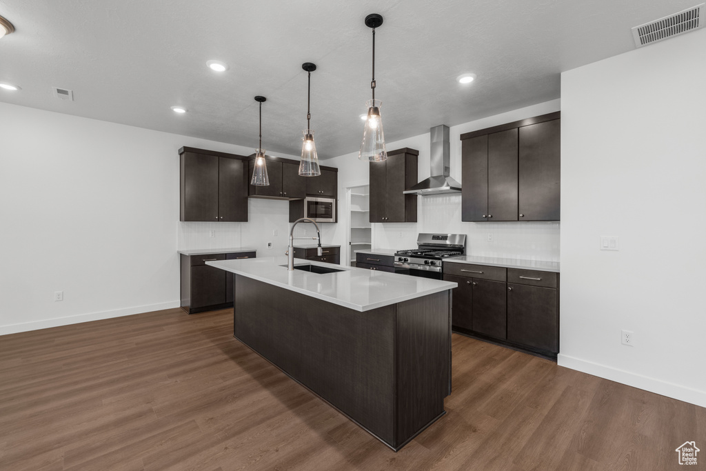 Kitchen featuring wall chimney exhaust hood, stainless steel appliances, a sink, baseboards, and recessed lighting