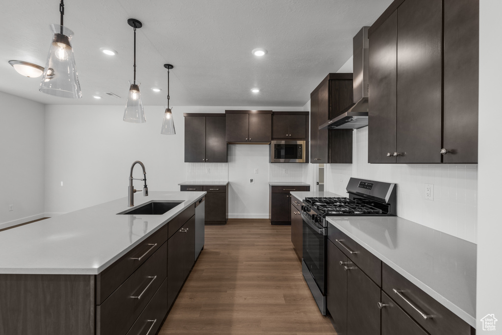 Kitchen with appliances with stainless steel finishes, a sink, wall chimney exhaust hood, dark wood-style flooring, and recessed lighting