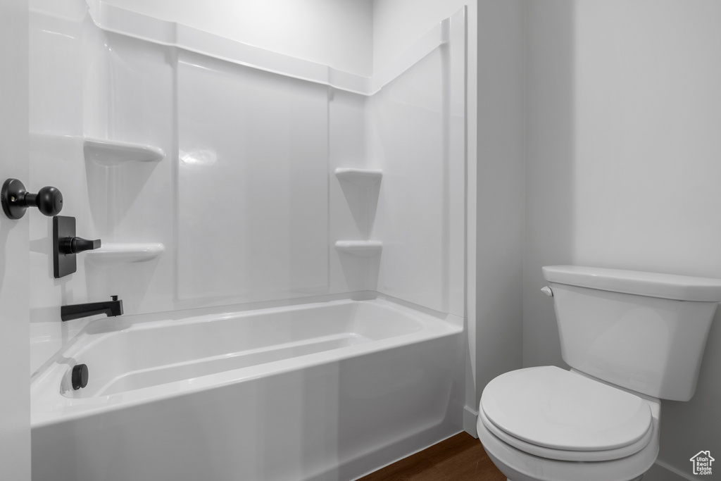 Full bathroom featuring toilet, wood finished floors, and washtub / shower combination
