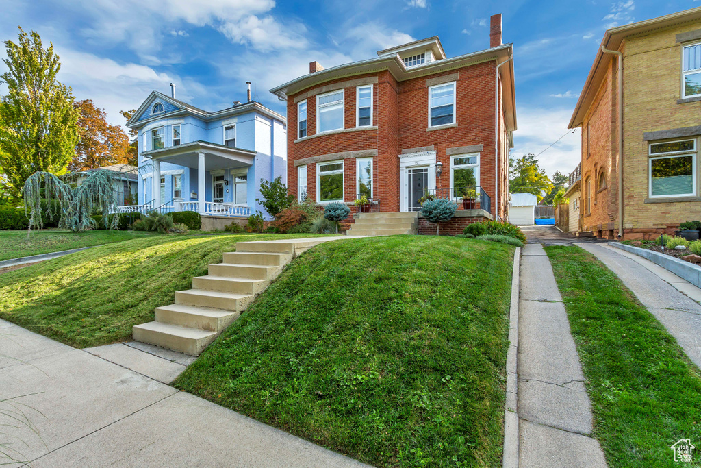 View of front of house with brick siding, a front lawn, a chimney, and covered porch