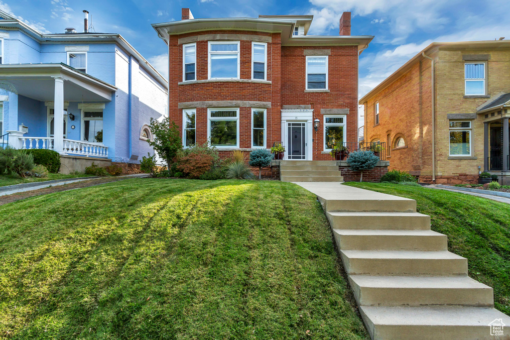 View of front of home featuring a chimney, brick siding, and a front yard