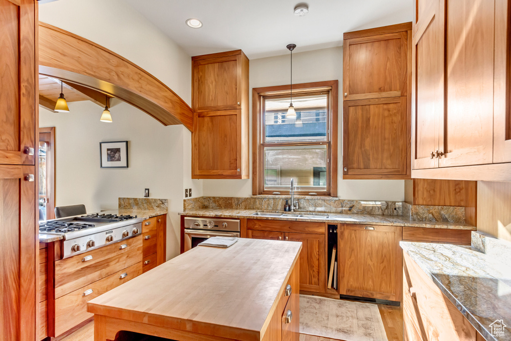 Kitchen featuring wooden counters, appliances with stainless steel finishes, light wood finished floors, a sink, and hanging light fixtures