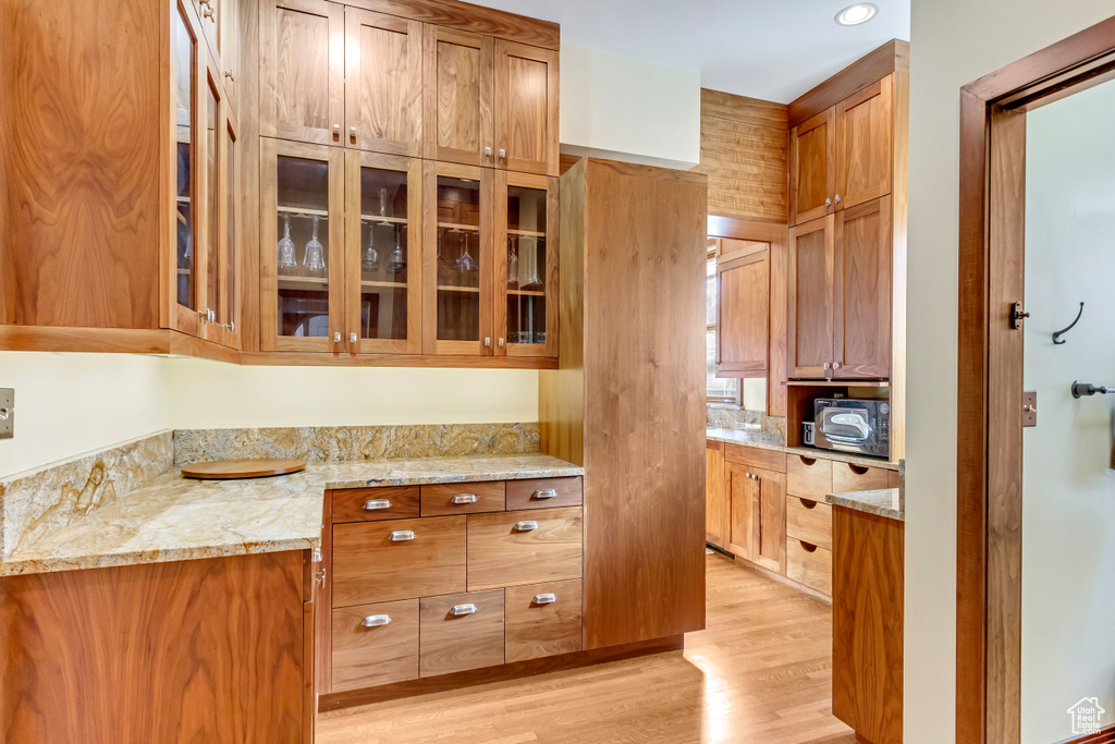Kitchen featuring light wood-style flooring, light stone counters, glass insert cabinets, and brown cabinetry
