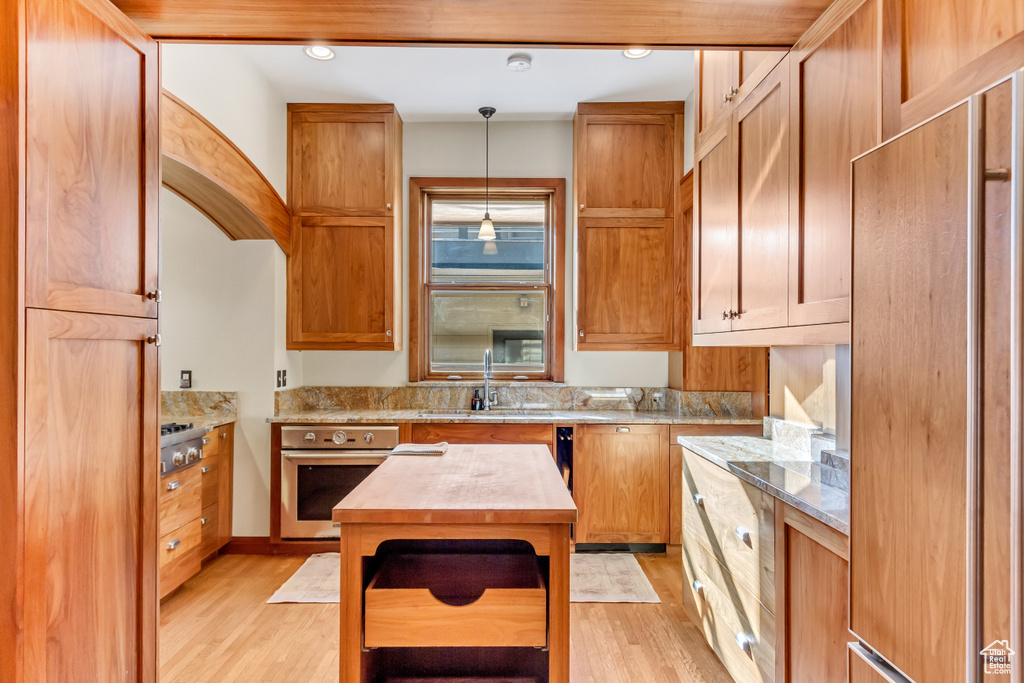 Kitchen with stainless steel appliances, light wood-type flooring, decorative light fixtures, and a sink