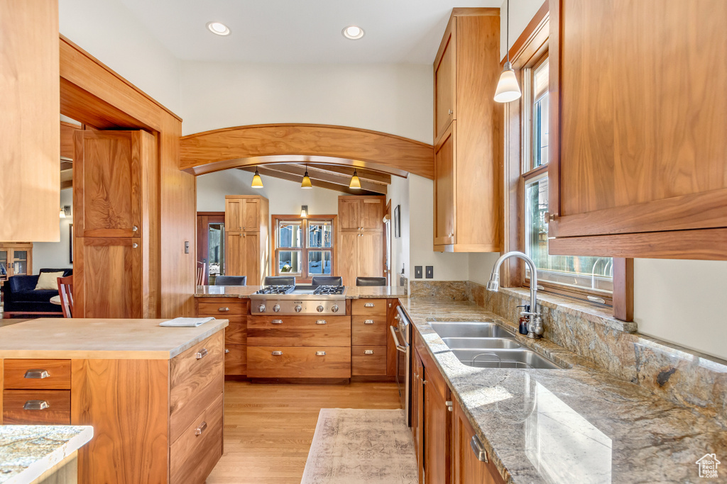 Kitchen with a sink, light wood finished floors, plenty of natural light, brown cabinetry, and lofted ceiling