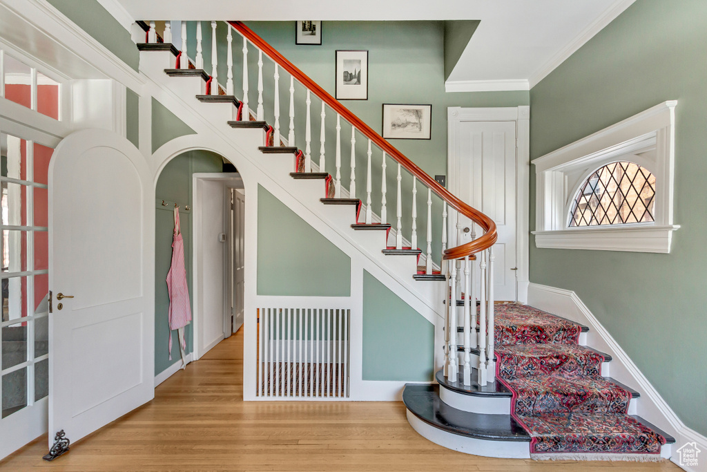 Stairs featuring arched walkways, crown molding, and wood finished floors