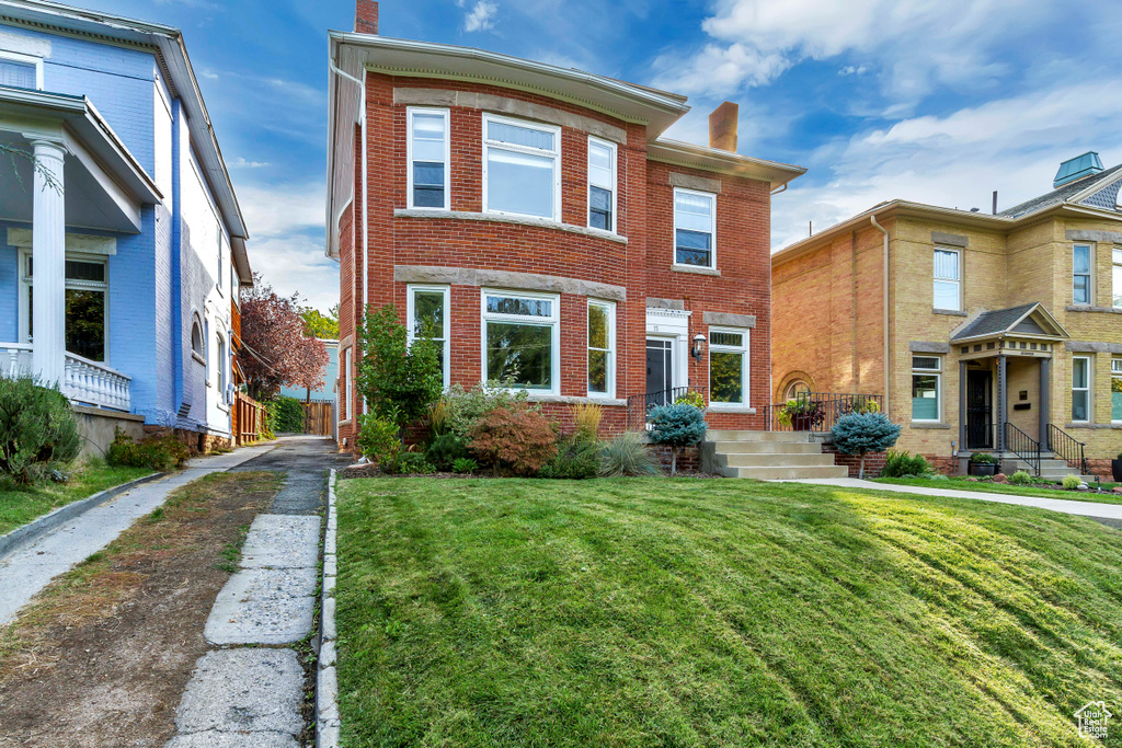 Townhome / multi-family property with a chimney, brick siding, and a front yard