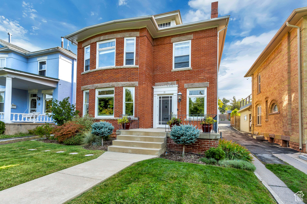 Multi unit property featuring brick siding, a front lawn, and a chimney