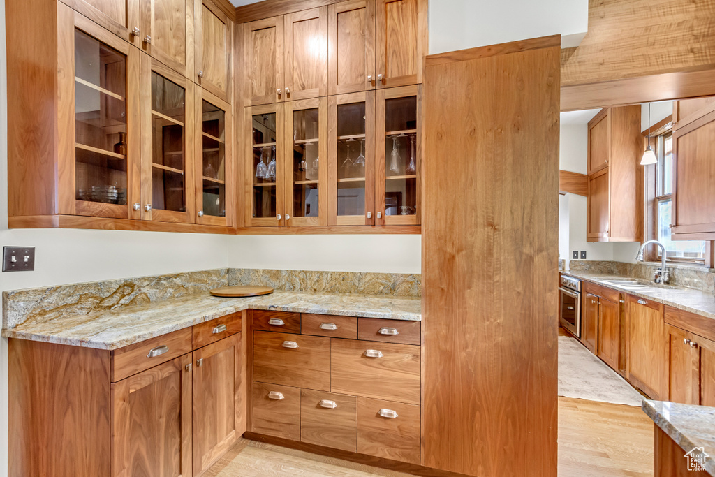 Kitchen with a sink, light stone counters, glass insert cabinets, and light wood-type flooring