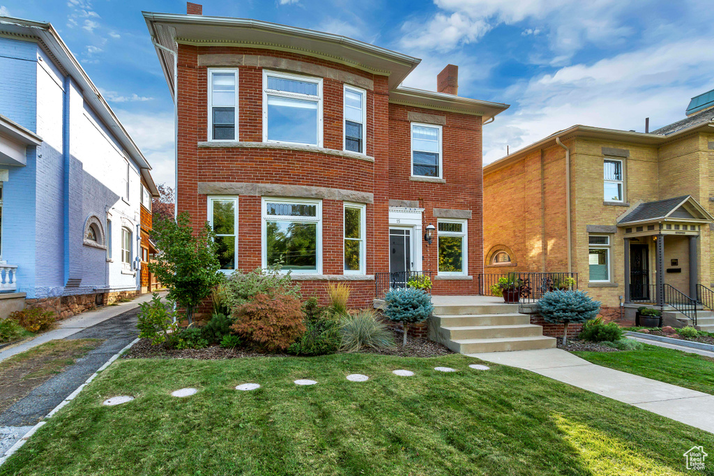View of front facade featuring a chimney, brick siding, and a front lawn