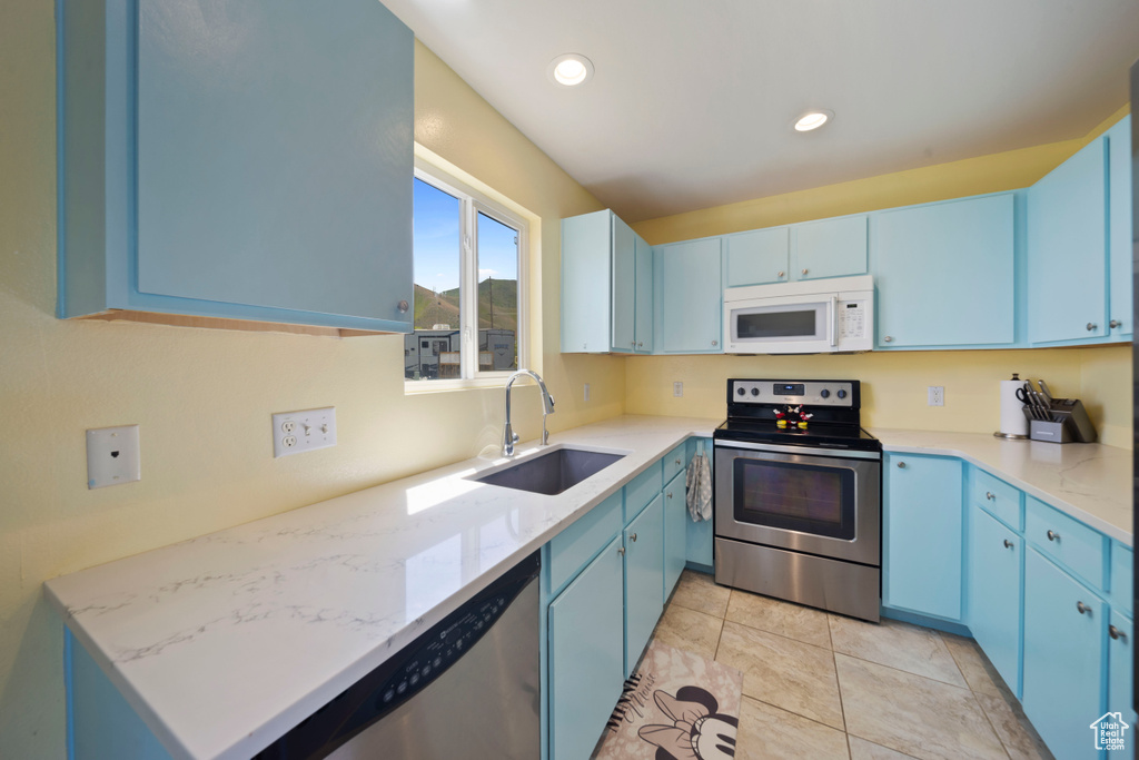 Kitchen featuring appliances with stainless steel finishes, blue cabinets, a sink, recessed lighting, and light stone counters