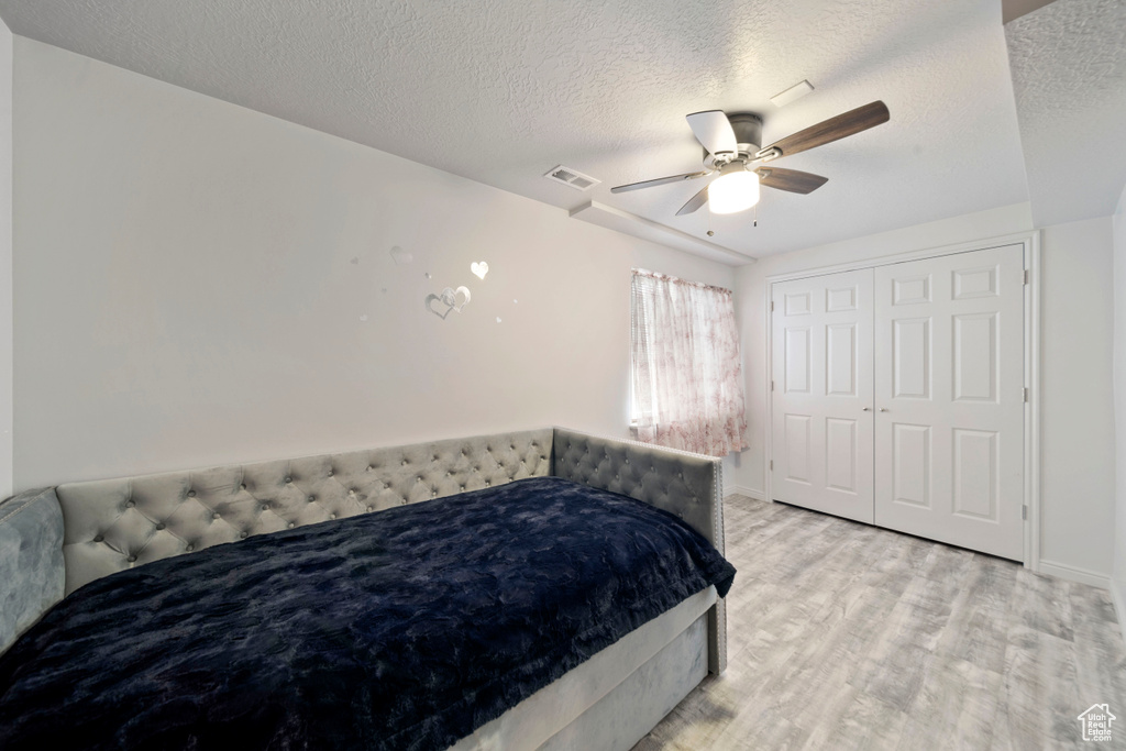 Bedroom featuring light wood-type flooring, a textured ceiling, ceiling fan, a closet, and baseboards