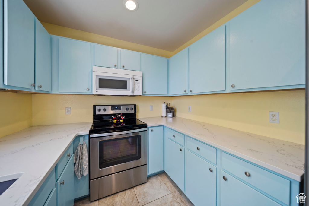 Kitchen with white microwave, stainless steel electric range, blue cabinets, and light stone countertops