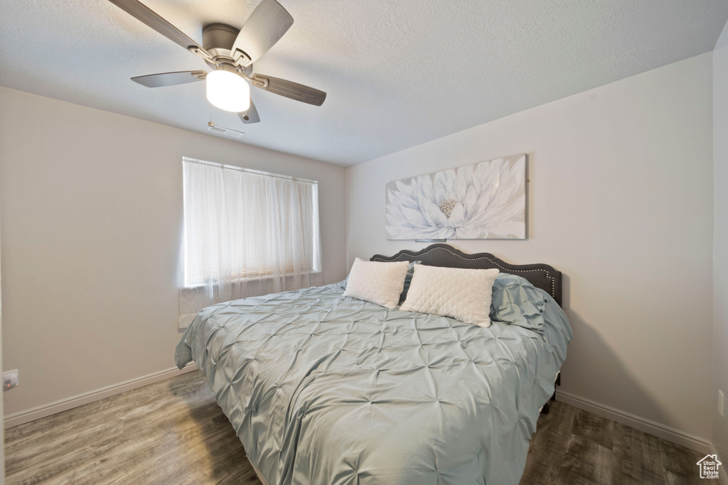 Bedroom with wood finished floors, baseboards, ceiling fan, and a textured ceiling