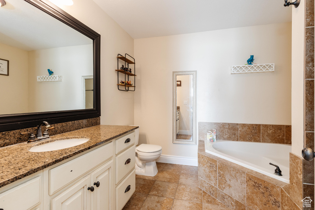 Bathroom with vanity, a bath, toilet, baseboards, and stone finish floors