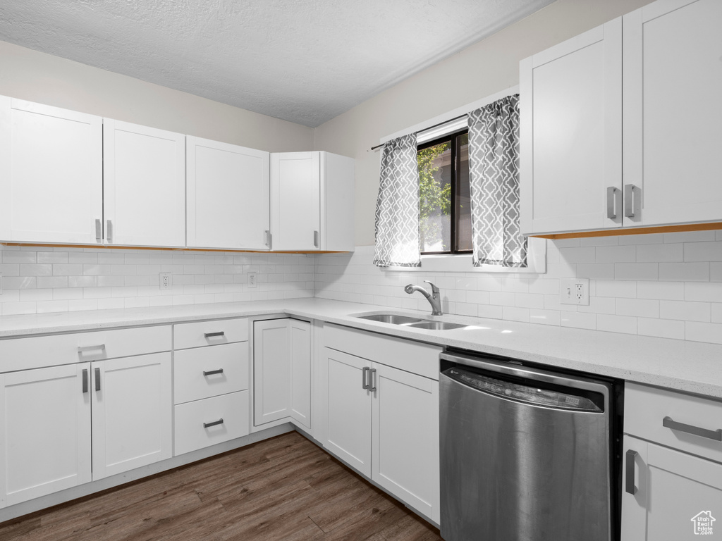 Kitchen with stainless steel dishwasher, a sink, light countertops, dark wood-type flooring, and white cabinetry