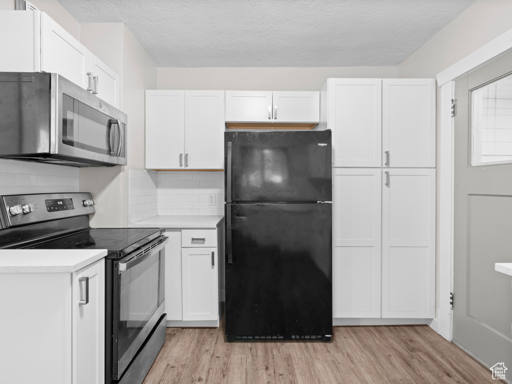 Kitchen featuring freestanding refrigerator, stainless steel microwave, electric range, light countertops, and light wood-type flooring