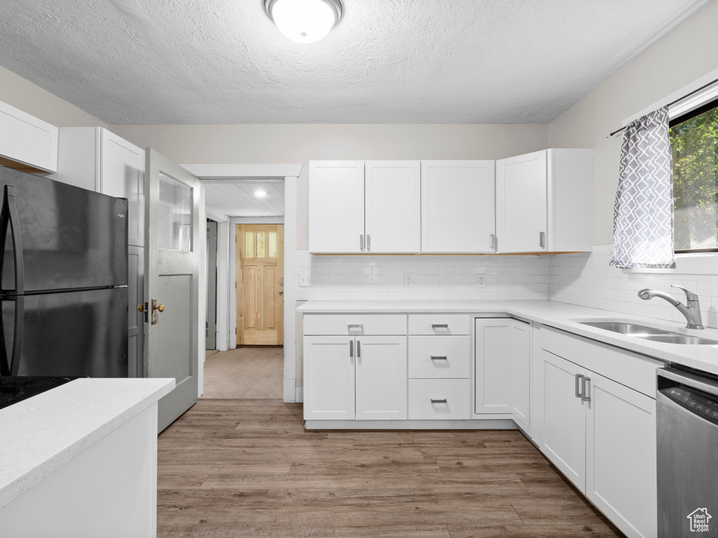 Kitchen with freestanding refrigerator, dishwasher, white cabinetry, and a textured ceiling