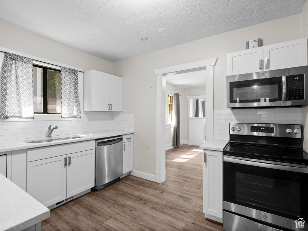 Kitchen with stainless steel appliances, a sink, backsplash, white cabinets, and a textured ceiling