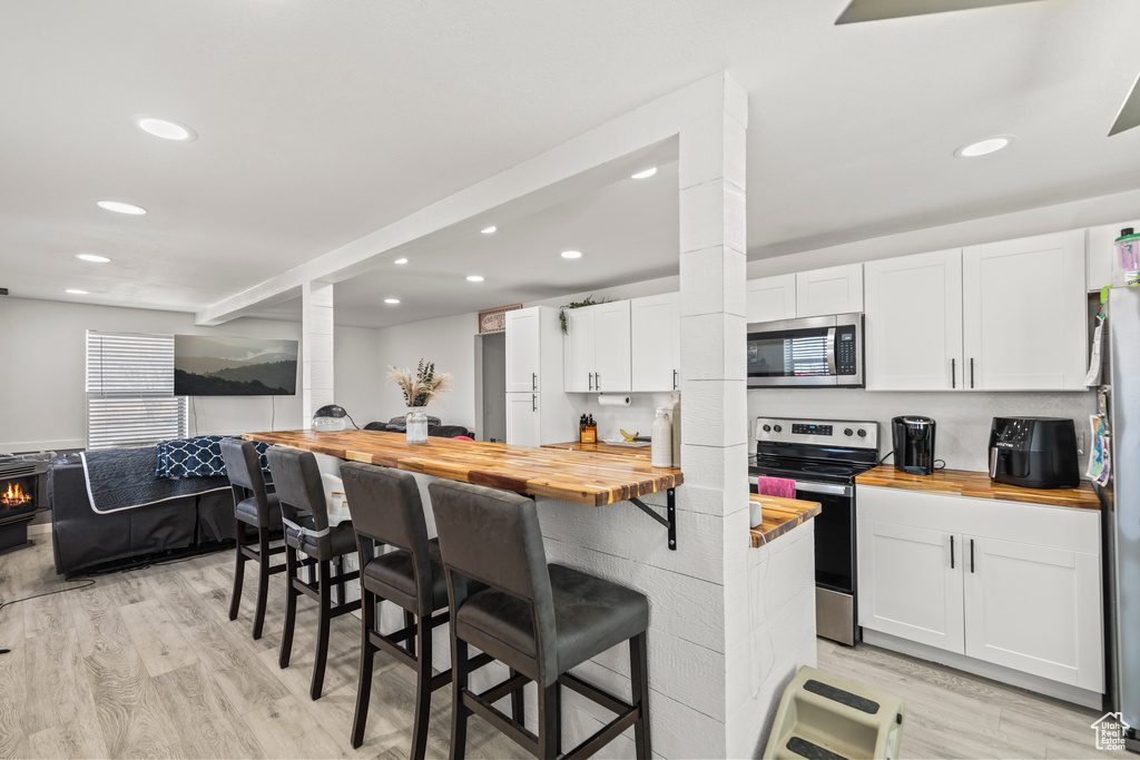 Kitchen featuring wooden counters, appliances with stainless steel finishes, recessed lighting, white cabinets, and light wood-style floors