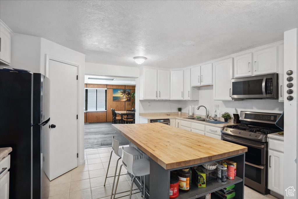 Kitchen with stainless steel appliances, wooden counters, a sink, a textured ceiling, and white cabinets