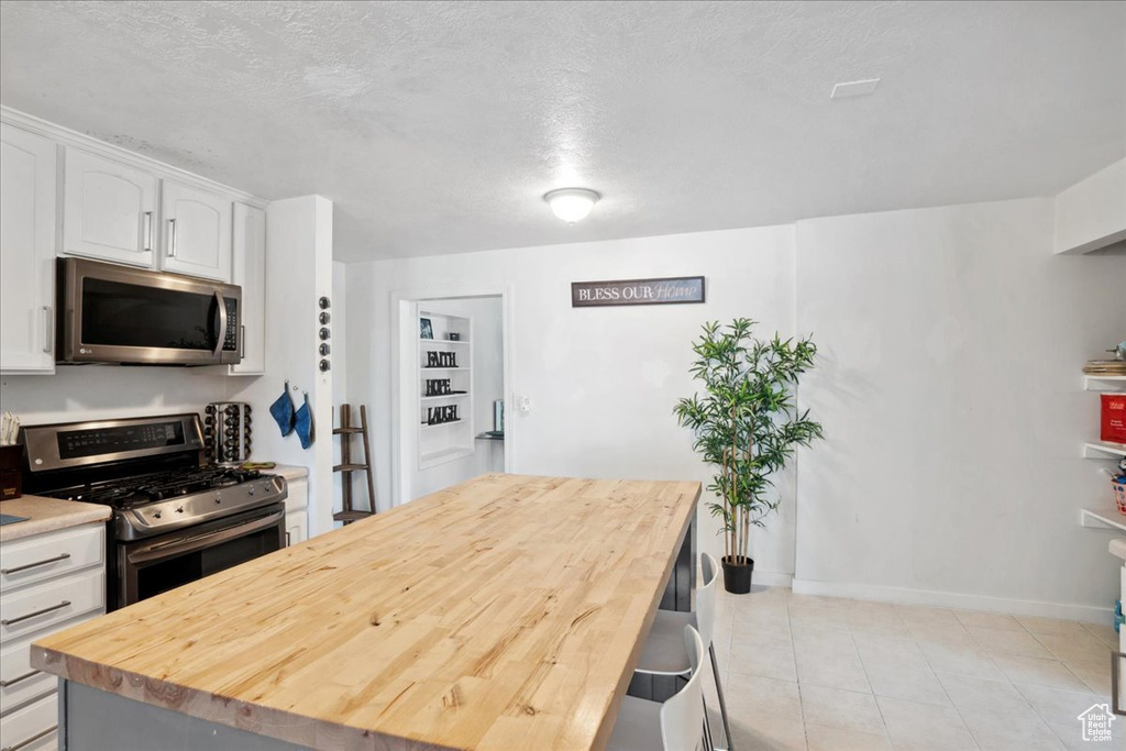 Kitchen with appliances with stainless steel finishes, white cabinetry, a kitchen island, wood counters, and light tile patterned floors