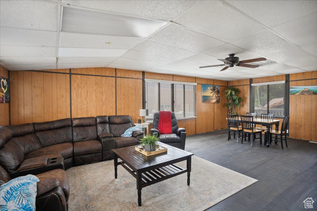 Living area with a paneled ceiling, wood walls, ceiling fan, and wood finished floors