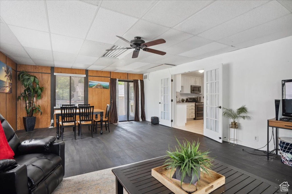 Living room featuring french doors, dark wood finished floors, wooden walls, a ceiling fan, and a paneled ceiling