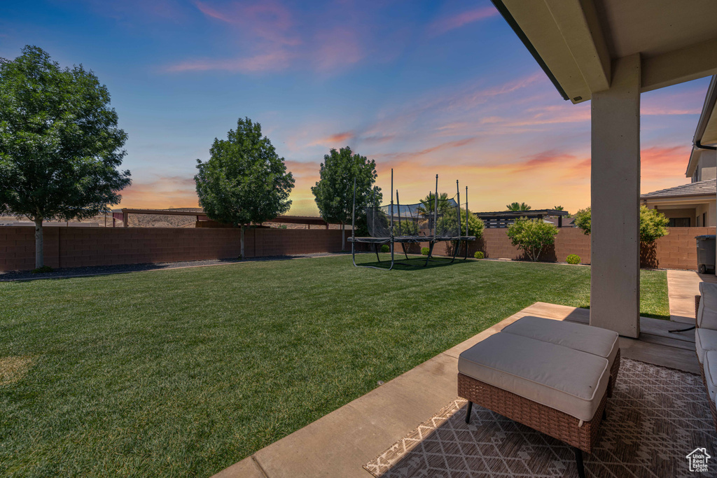 Yard at dusk featuring a trampoline and a patio