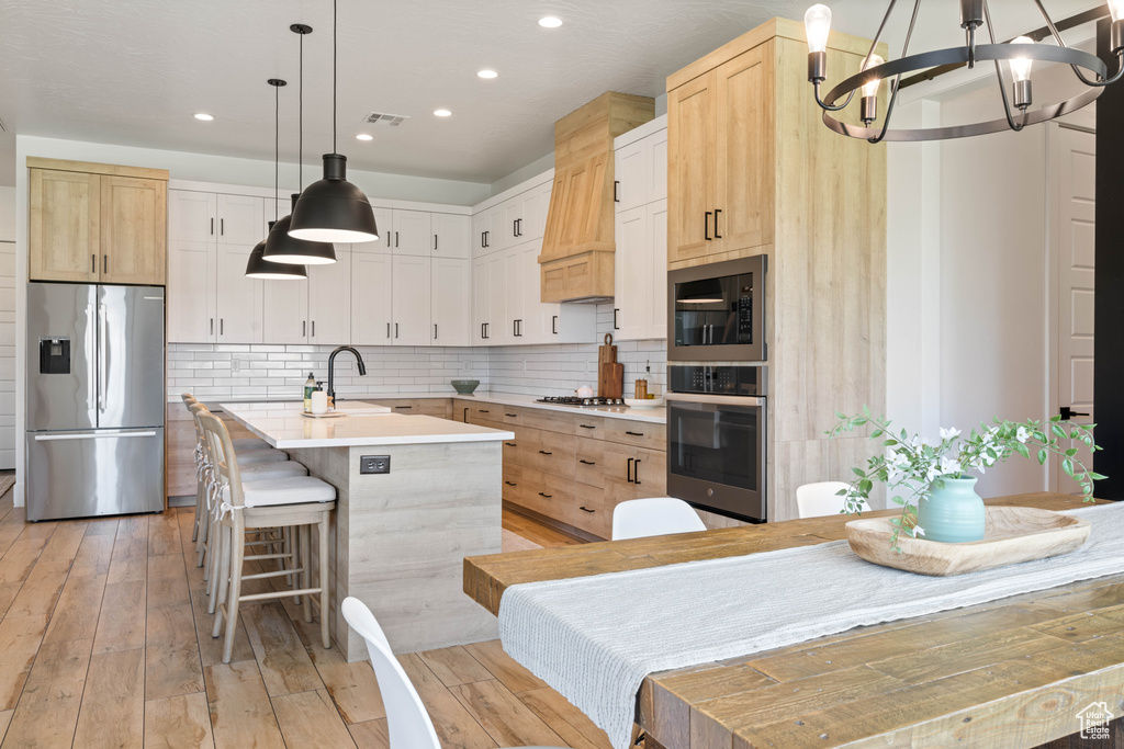 Kitchen with stainless steel appliances, a chandelier, a kitchen island with sink, recessed lighting, and light countertops