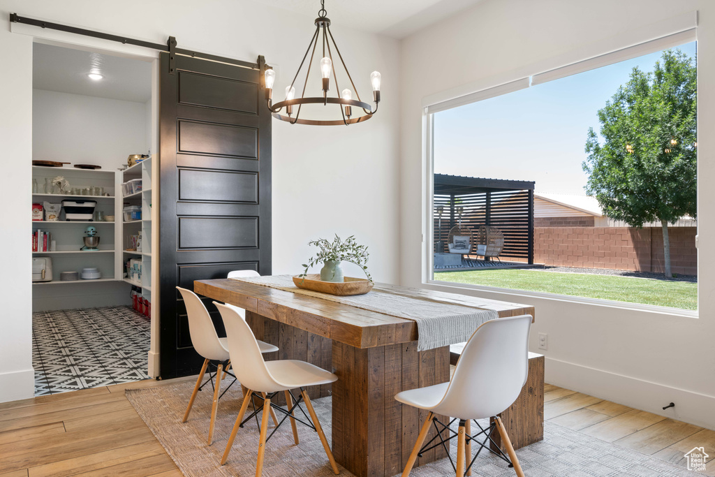 Dining room with a barn door, wood finished floors, a chandelier, and healthy amount of natural light