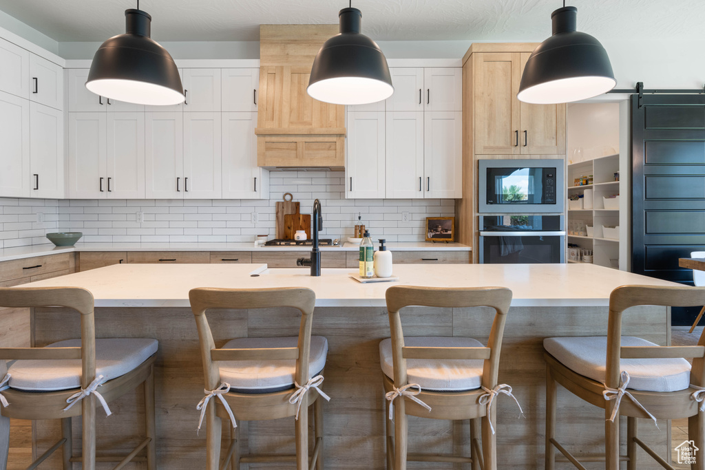 Kitchen with stainless steel appliances, decorative backsplash, light countertops, a kitchen island with sink, and a breakfast bar