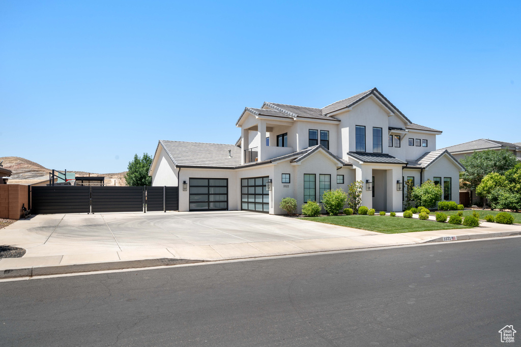 View of front of house with an attached garage, driveway, a gate, stucco siding, and a standing seam roof
